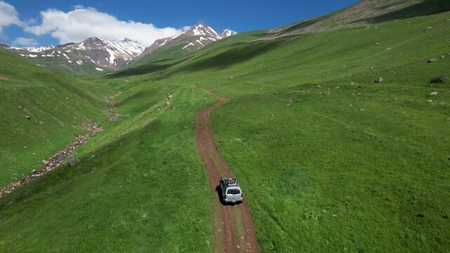 Drone follows an SUV going up the slope of Mount Aragats along Gagharot river on sunny summer day. Armenia.
