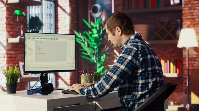 Man in home office looking at UI on PC screen, typing and executing programming code. Coding application UI used by IT developer writing and testing code in modern workspace, camera B