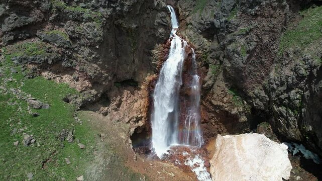 Orbital aerial shot of Gagharot waterfall with rainbow on sunny summer day. Mount Aragats, Armenia.