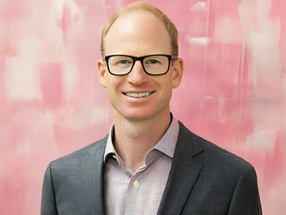 A professional portrait of a man against a pink backdrop.