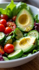 Macro shot of fresh salad bowl with mixed greens, cherry tomatoes, sliced cucumbers, and avocado drizzled with vinaigrette