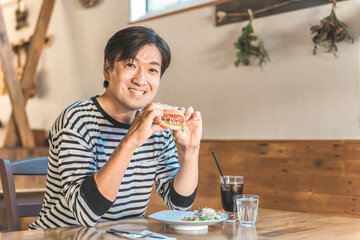 お昼休みにカフェやレストランでハンバーガーを食べるアジア人の男性
