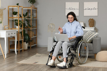 Young woman in wheelchair with headphones using laptop at home