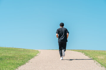 青空の下でランニング・ジョギングをする男性（アスリート・有酸素運動・ワークアウト・フィットネス）

