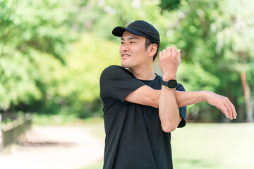 新緑の公園でストレッチをするスポーツウェア姿のアジア人男性
