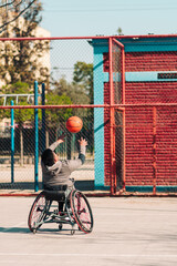 Obraz premium Young Latino athlete in wheelchair, training, playing and concentrating with basketball in a city park outdoors