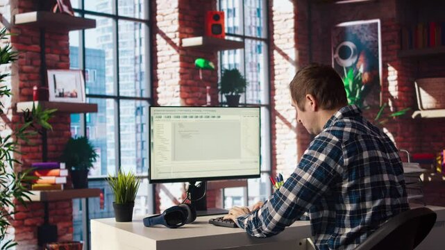 Man in home office looking at UI on PC screen, typing and executing programming code. Coding application UI used by IT developer writing and testing code in modern workspace, camera A