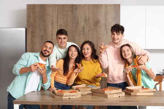 Group of young friends eating pepperoni pizza in kitchen