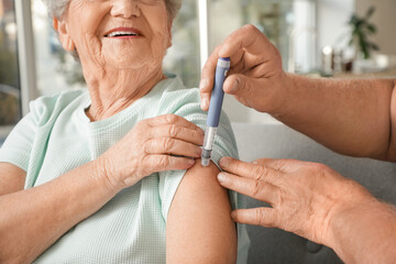 Diabetic senior woman with her husband using lancet pen at home, closeup