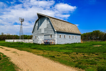 A large, old-fashioned barn sits in a field with a dirt road leading to it