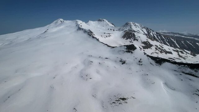 Forward reveal aerial shot of Mount Aragats cowered with snow on sunny spring day. Armenia.