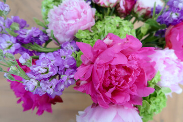 A vibrant floral arrangement featuring bold pink peonies, delicate purple blossoms, and fresh green accents, creating a lively and colorful composition with a softly blurred background.