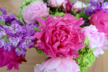 A vibrant bouquet featuring a bold pink peony surrounded by soft purple and pastel pink blossoms, accented with fresh green foliage, creating a lively and elegant floral arrangement.