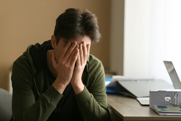 Depressed young man sitting near table at home