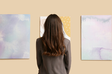 Young woman near paintings on beige wall in art gallery, back view