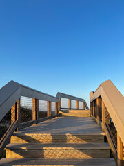 A wooden boardwalk stairway leads upward under a vibrant blue sky bathed in warm evening sunlight with soft shadows creating a peaceful and inviting atmosphere