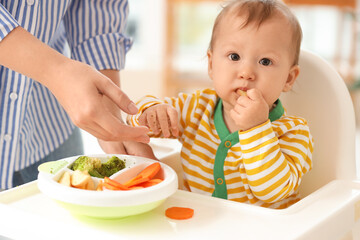 Mother feeding her little baby in high chair at home, closeup