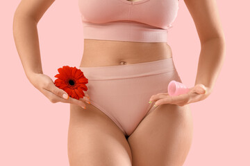 Young woman in panties with red flower and menstrual cup on pink background, closeup
