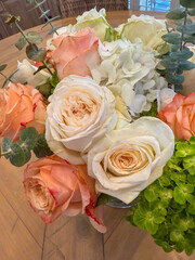 A soft arrangement of peach-orange roses with layered petals, placed in a simple vase on a wooden table, exuding warmth and elegance in a cozy indoor setting.