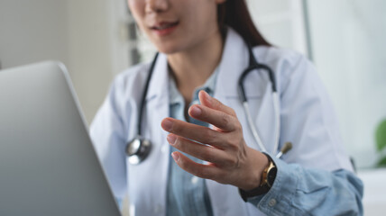 Telemedicine concept. Asian woman doctor talking to online patient on laptop computer sitting at...