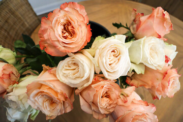 A stunning arrangement of peach-orange and white roses, their delicate petals layered in soft spirals, surrounded by lush green leaves, placed on a wooden table for an elegant floral display.