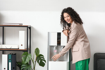 Beautiful businesswoman taking glass from water cooler in office