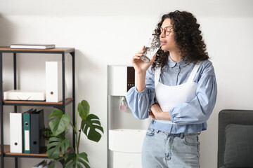 Young woman drinking water from cooler in office