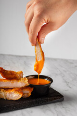 Hand Picking Up a Chicken Tender from a Ramekin with Yellow Sauce