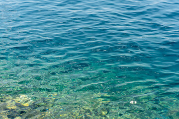 Vivid turquoise seawater with crystal-clear transparency, sunlit reflections, and visible underwater rocks. Concept of coastal serenity, natural beauty, and untouched marine environment.
