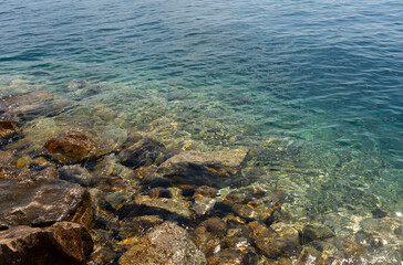 Crystal-clear turquoise sea water with rocky shoreline on a sunny summer day. Concept of coastal beauty, tranquility, and the natural charm of marine landscapes.
