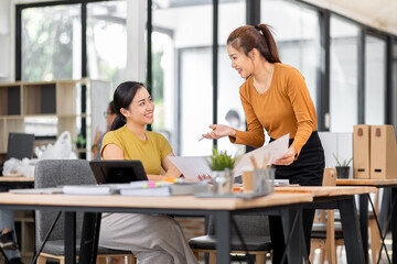 Happy two asian female freelance entrepreneurs reading and planning analyzing the financial report, business plan investment,  on computer while working together in the office.

