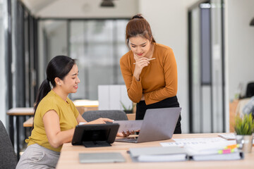 Happy two asian female freelance entrepreneurs reading and planning analyzing the financial report, business plan investment,  on computer while working together in the office.
