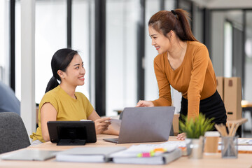 Obraz premium Happy two asian female freelance entrepreneurs reading and planning analyzing the financial report, business plan investment, on computer while working together in the office. 