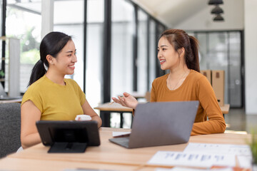 Happy two asian female freelance entrepreneurs reading and planning analyzing the financial report, business plan investment,  on computer while working together in the office.
