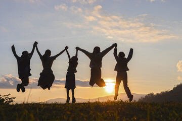 Silhouette of happy children jumping playing on mountain at sunset time