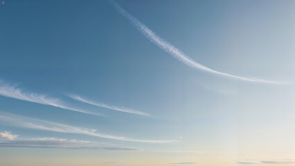 Soft blue sky with wispy clouds and delicate contrails at sunset