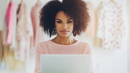 Fashion designer focused on laptop, surrounded by vibrant fabrics and sketches in a bright studio environment