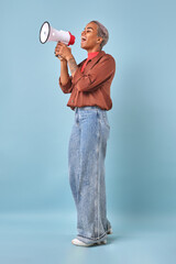 Confident African American individual stands on a light blue backdrop, joyfully using a megaphone to inspire others.