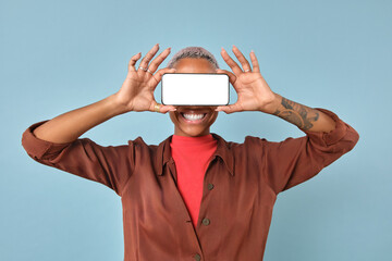 African American person with joyful smile holds up a smartphone in front of their face, set against a vibrant blue background. Their playful demeanor captures a moment of fun and spontaneity.