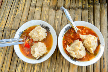 the delicious Two Mie Pentol Bakso or meatball soup in the White bowl with spoon and fork . Two Traditional Food of a Bakso Indonesian .Focus on meatball, Noisy, exposure, similar others