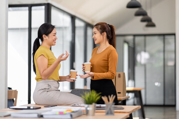 Fototapeta premium Two asian happy businesswomen talking during coffee break in modern office or coworking space. relaxing and talking after working time, business and people partnership concept 