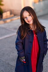 Fototapeta premium Pretty caucasian 6 year old girl with brown hair and freckles smiles in her red velvet holiday dress and navy blue coat