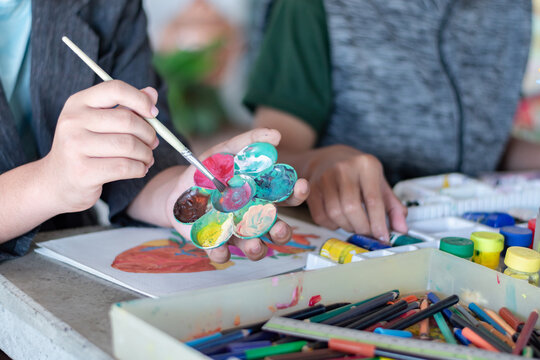 Learning to use poster color to draw various pictures of asian boys on a table outside classroom with his female art teacher, raising teen and adult helps kids school project concept.