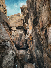 A vibrant photo of steep rock formations forming a narrow canyon against a bright blue sky, showcasing the warm hues and rugged textures of the stone.