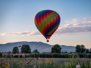 Obraz premium Hot Air Balloon Over Scenic Meadow and Mountains at Sunrise