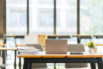 Laptop Computer, notebook, and eyeglasses sitting on a desk in a large open plan office space after working hours	