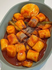 Spicy Korean tteokbokki with chewy rice cakes in a vibrant red sauce, topped with sesame seeds and green onions. A popular street food known for its addictive flavor and satisfying texture.
