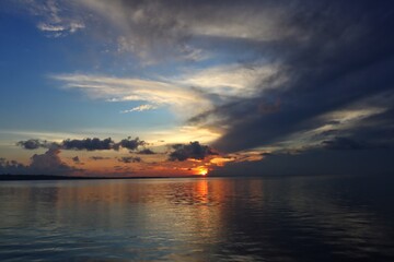 Stunning views of the sun setting over the calm ocean, under a dramatic sky.