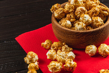 Snack, movie concept, caramelized popcorn in a wooden bowl on a red napkin