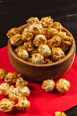 Caramelized popcorn in a wooden bowl on a red napkin on a wooden table